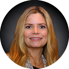 Professional headshot: smiling woman with long blonde hair, wearing a blazer, against a dark gradient background.