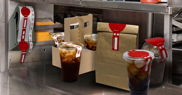 Assorted iced drinks in plastic cups with red-labeled lids and brown takeout boxes on a stainless steel counter in a kitchen area. Order security with Lined Labels